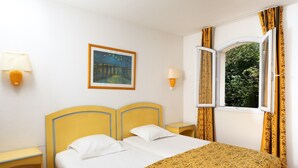 Une chambre d’hôtel avec un lit, deux tables de chevet, une commode, une fenêtre avec des rideaux et un tableau au mur.