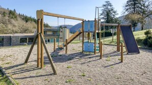 A playground with swings and a slide, surrounded by a gravel area with sparse vegetation. - Appartement au Calme! Balcon avec Vue + Piscine (Miremont)