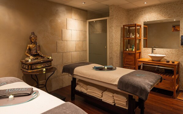 Un tranquilo espacio de spa con una estatua de meditación, una camilla de masaje, un mueble de madera con artículos de aseo y un espejo grande.