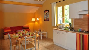 Una cocina compacta con armarios blancos, un comedor con una mesa lista para dos personas y un ventanal que proporciona luz natural.