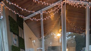 An outdoor patio with a sofa, chairs, and a table. There are string lights, greenery, and a view through large windows. - Charming 2-bedroom cottage in Clarington with hottub, WiFi and AC (Clarington)
