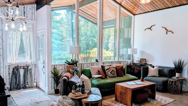 A cozy living room with a green sofa, wooden coffee table, and a large window offering a view of greenery. - Charming 2-bedroom cottage in Clarington with hottub, WiFi and AC (Clarington)