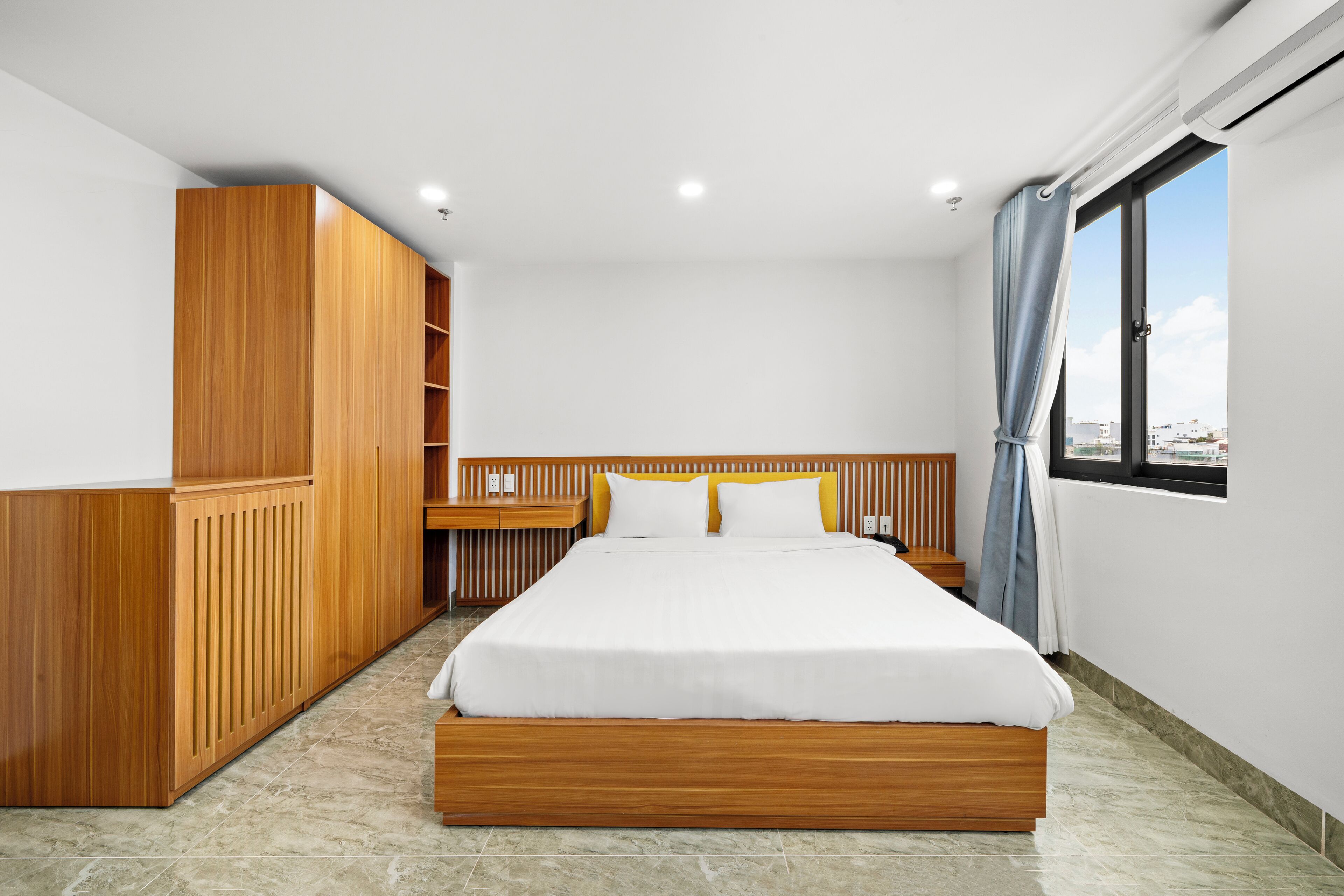 Un dormitorio moderno con estructura de cama de madera, ropa de cama blanca y vistas a la ciudad a través de una ventana.