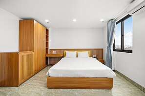 Un dormitorio moderno con estructura de cama de madera, ropa de cama blanca y vistas a la ciudad a través de una ventana.