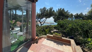 A terrace with a glass wall overlooking a scenic coastal view, outdoor furniture, and a stone pathway. - Le Paradis Marin (Saint-Cyr-sur-Mer)