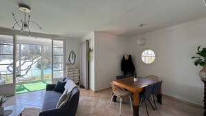 A spacious living area with a large window, a dining table with chairs, a sofa, and a ceiling light fixture. - Le Paradis Marin (Saint-Cyr-sur-Mer)