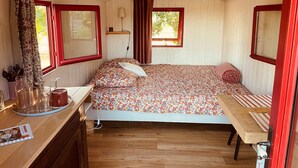 A cozy, compact room with a bed, a small table, and a window. - La Roulotte (2 people) (Pillac)
