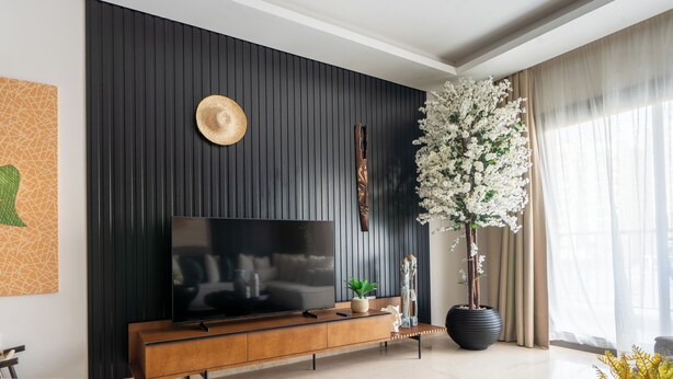A modern living room with a large flat-screen TV on a wooden console, a decorative wall panel, and a large potted plant. - Apartment in El Sheikh Zayed (Giza Governorate)