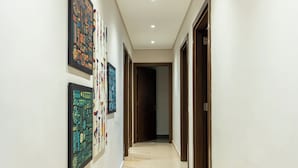 A hallway with three framed artworks on the left wall, leading to a dark room at the end. - Apartment in El Sheikh Zayed (Giza Governorate)