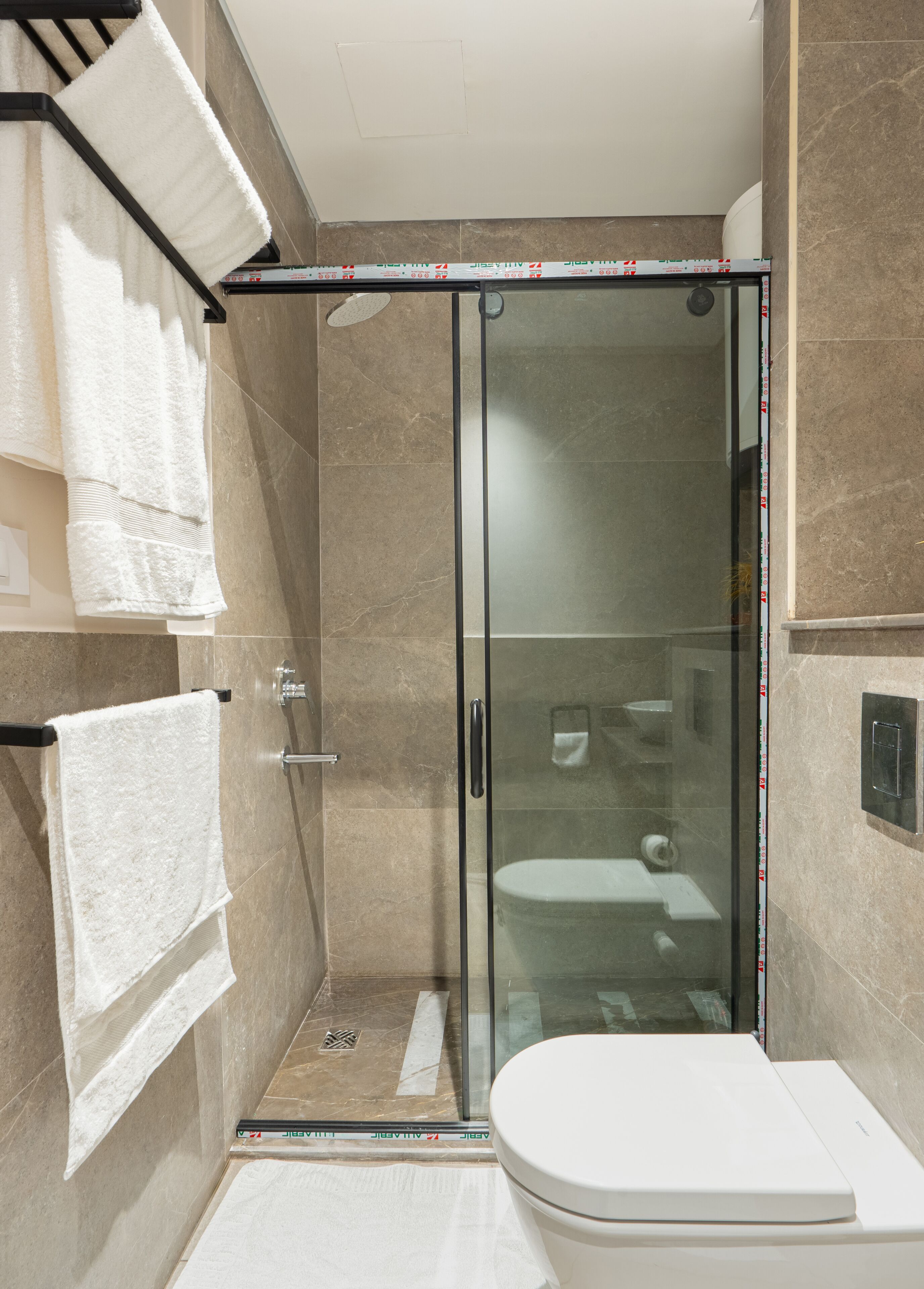 A modern bathroom with a glass-enclosed shower, a white toilet, and multiple white towels hanging on a rack.