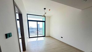 A spacious room with a large window, wooden flooring, and a modern light fixture.