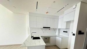A modern kitchen with white cabinetry, a marble countertop, and a light wood floor.