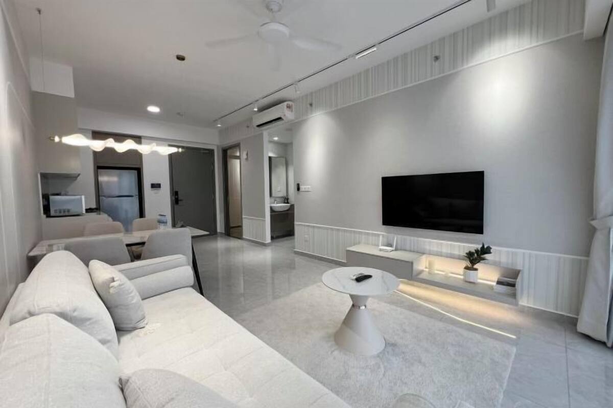 A modern living room with a sofa, a round coffee table, a flat-screen TV mounted on the wall, and a ceiling fan.