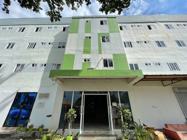 A multi-story building with a green and white facade, a glass entrance, and potted plants in front. - Stay Inn Mactan (Cordova)