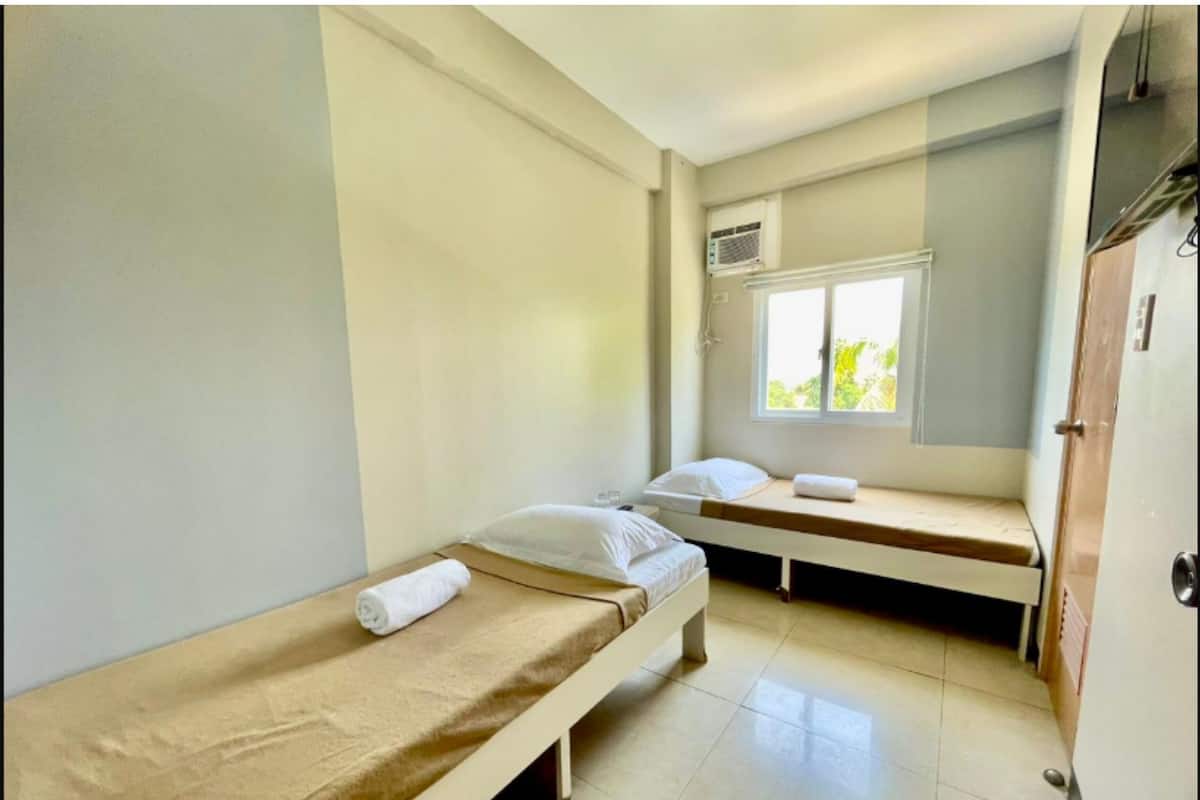 Une petite chambre propre, avec deux lits simples, une fenêtre donnant sur un beau paysage et un appareil de climatisation.