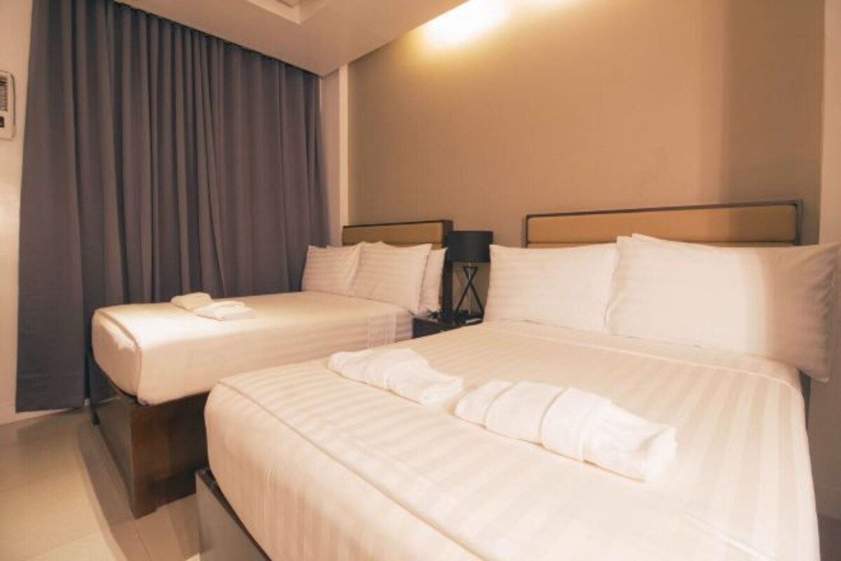 Habitación de hotel con dos camas, una mesita de noche, una lámpara y un ventanal con cortinas.