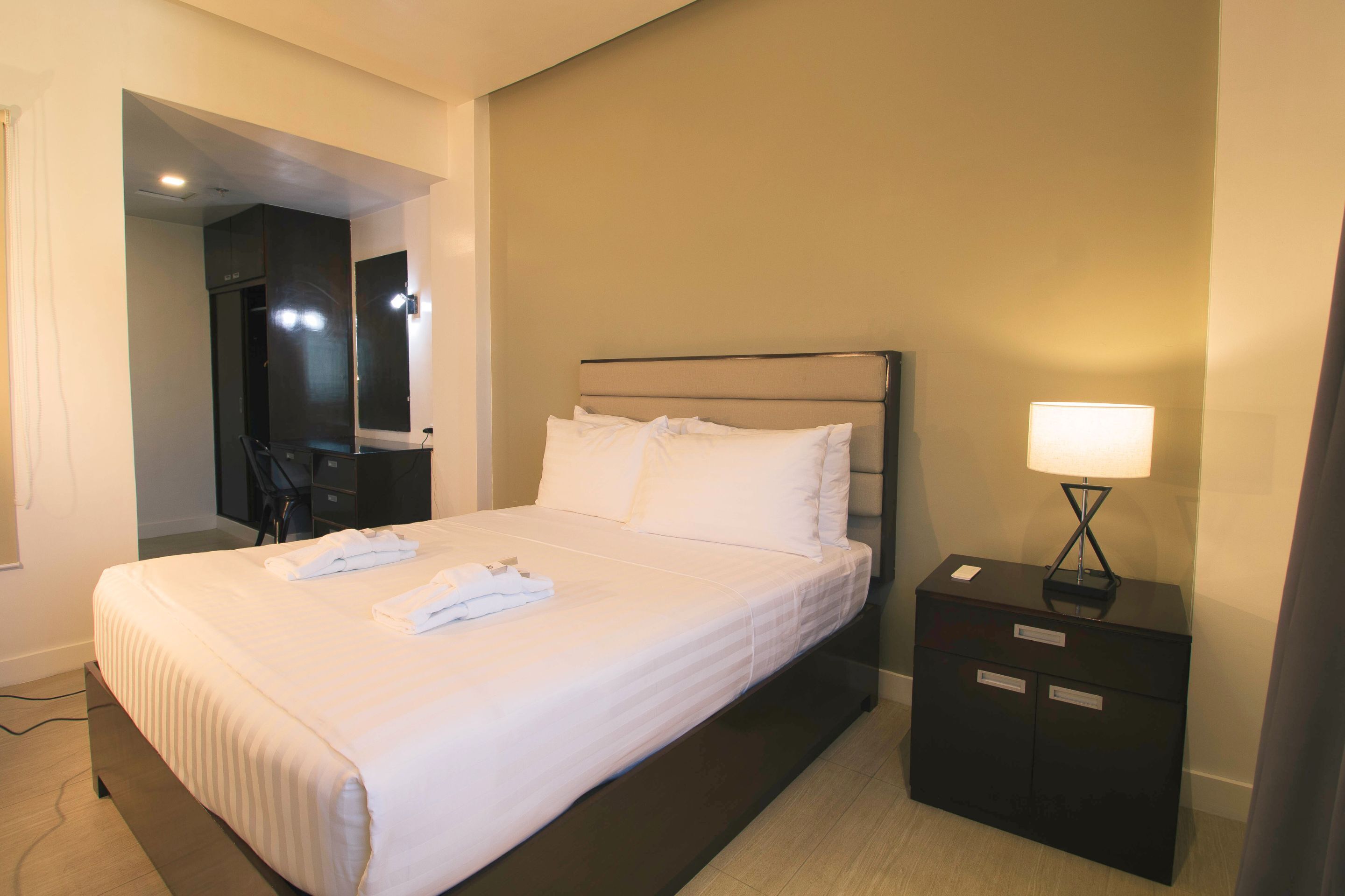 A hotel room with a bed, a nightstand, a lamp, and a mirror.