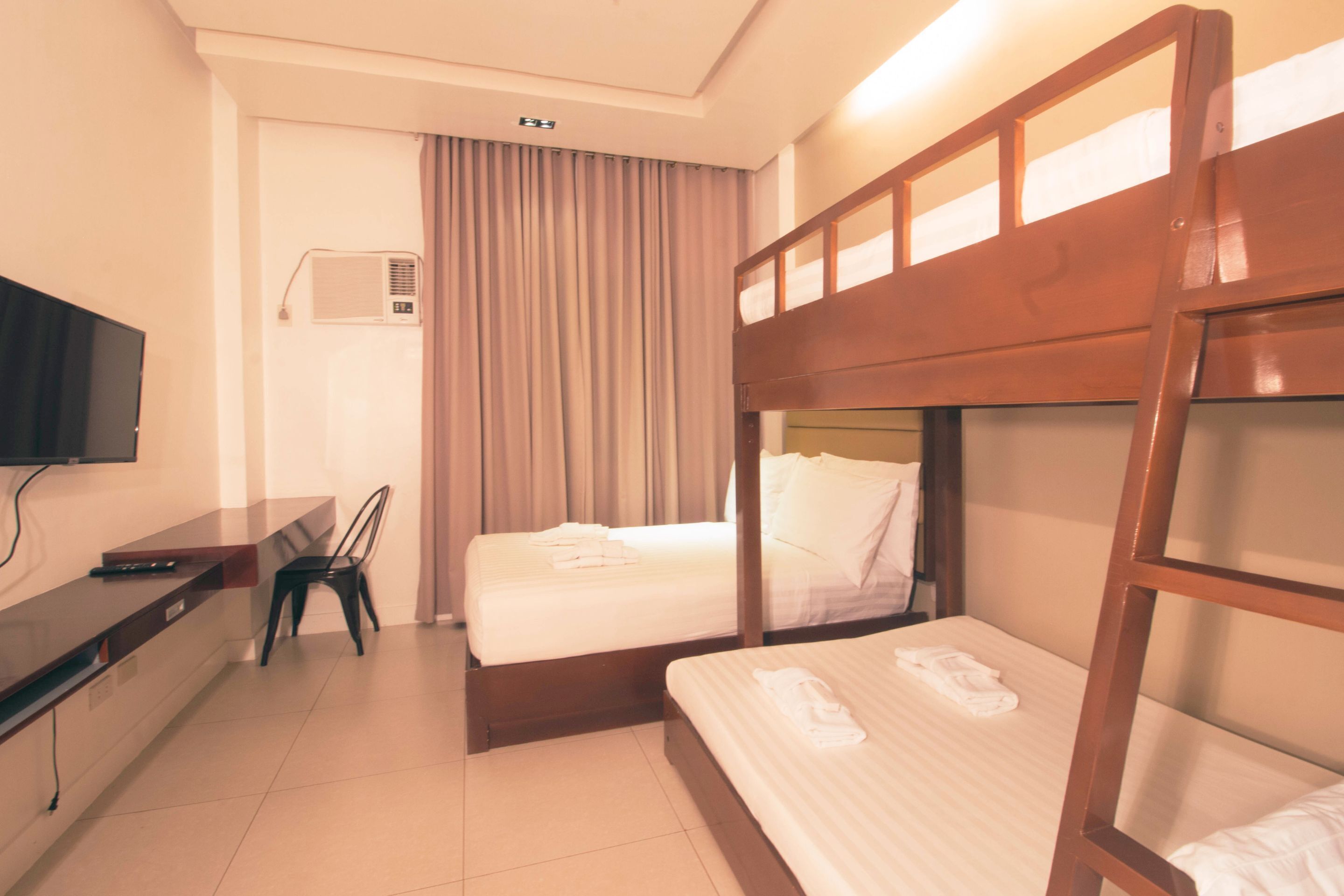Une chambre d’hôtel avec des lits superposés, un bureau avec une chaise, une télévision et une fenêtre avec des rideaux.