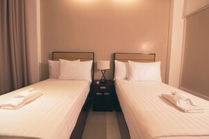 Habitación de hotel con dos camas individuales, una mesita de noche con lámpara y una ventana con cortinas.