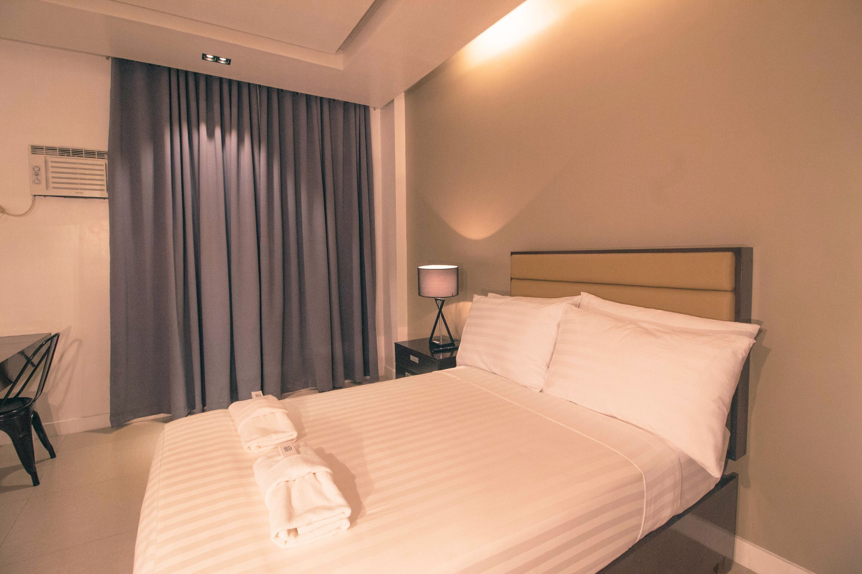 Ein ordentlich bezogenes Bett mit weißen Leinen, eine Nachttischlampe und ein Sessel in einem Hotelzimmer.