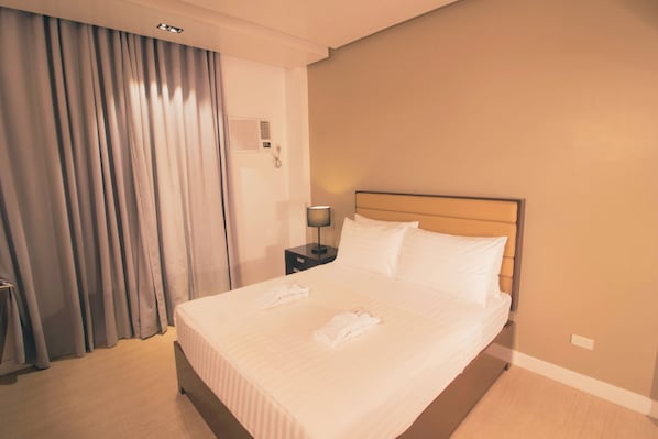 A hotel room with a large bed, a nightstand with a lamp, and a window with curtains.