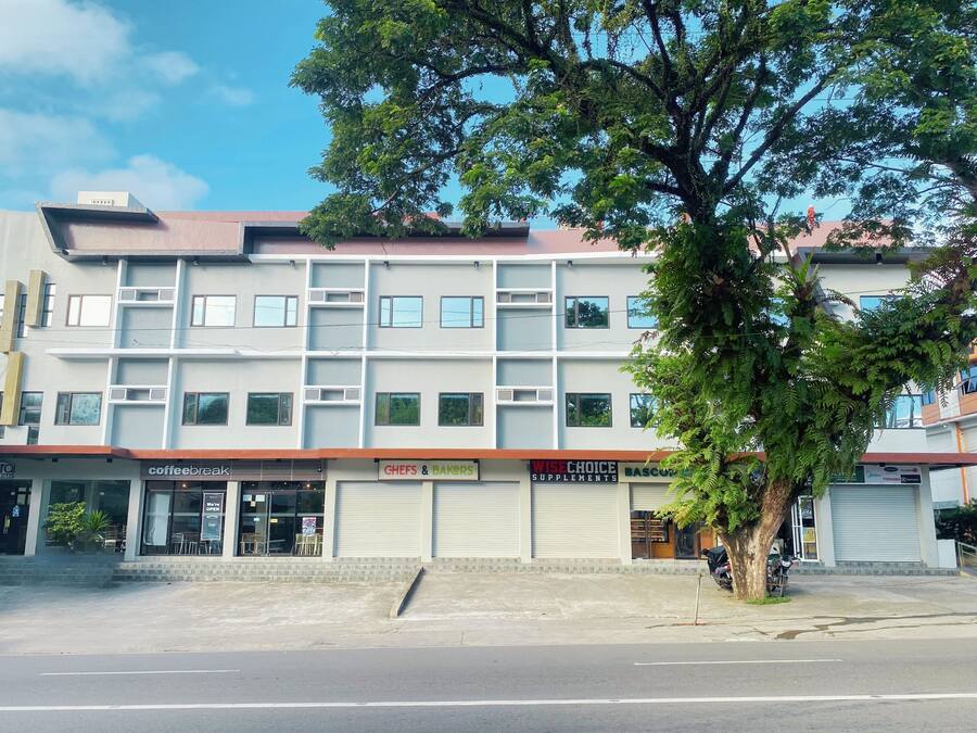 A multi-story building with various commercial establishments on the ground floor, including a coffee shop, a bakery, and a health supplements store.