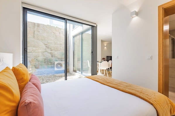 A bedroom with a bed, a sliding glass door leading to a patio, and a dining area visible through the door.