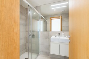 A modern bathroom with a glass shower enclosure, a white vanity with a mirror, and a wooden door.
