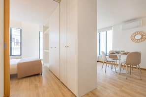 A modern, well-lit room with a dining area, a sofa, and a large window.