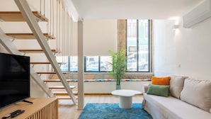 A modern living room with a staircase, a flat-screen TV, a sofa, and a large window with a view of the street. - Duque de Saldanha Residences (Porto)