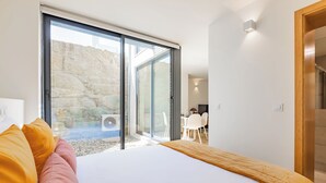 A bedroom with a large bed, a sliding glass door leading to a patio, and a dining area visible through the door. - Duque de Saldanha Residences (Porto)