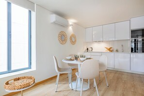 Une cuisine moderne avec des meubles blancs, une table de salle à manger ronde entourée de chaises et une grande fenêtre.