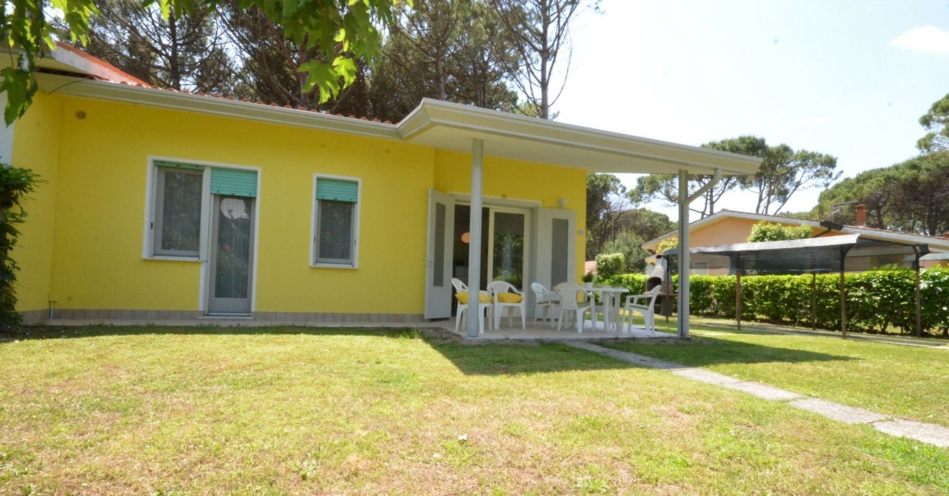 A yellow building with a covered patio area, white chairs, and a small garden.
