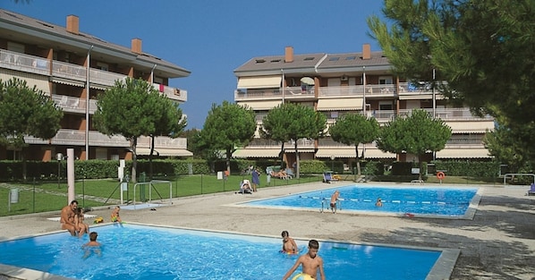 Zona de piscinas con varias albercas, rodeada de edificios de apartamentos con balcones.