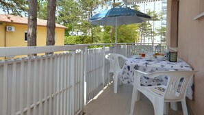 A balcony with a white railing, a table with a white tablecloth, and a blue umbrella. - Sweet retreat between pines and waves in Lignano (Lignano Sabbiadoro)