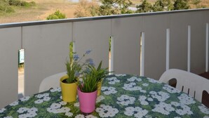 A balcony with a view of the beach and ocean, a table with a floral tablecloth, and two potted plants. - Adorable seaside holiday home (Bibione)
