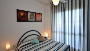 A bedroom with a bed, striped curtains, a ceiling fan, and a nightstand with a lamp. - Adorable seaside holiday home (Bibione)