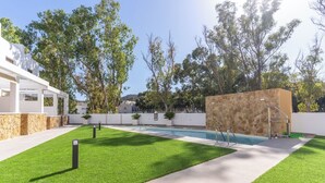 A modern outdoor pool area with a stone wall, a concrete pathway, and green grass.