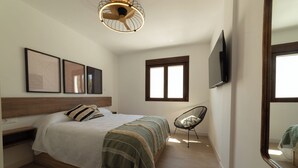 A bedroom with a bed, a chair, a TV, and framed artwork on the wall.