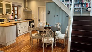 A modern kitchen with a dining area, wooden flooring, and a staircase leading to a book-filled loft.
