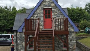 A stone cottage with a red door, wooden balcony, and a chimney.
