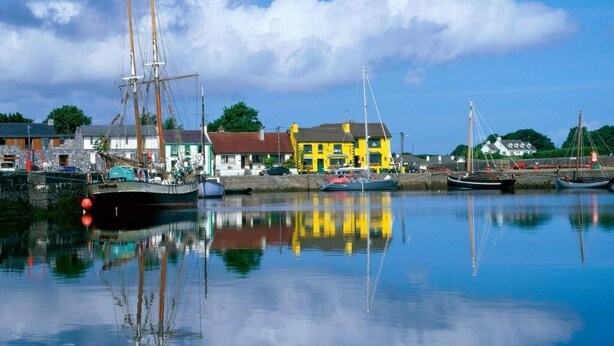 A harbor with boats, a yellow building, and a calm water surface reflecting the sky.