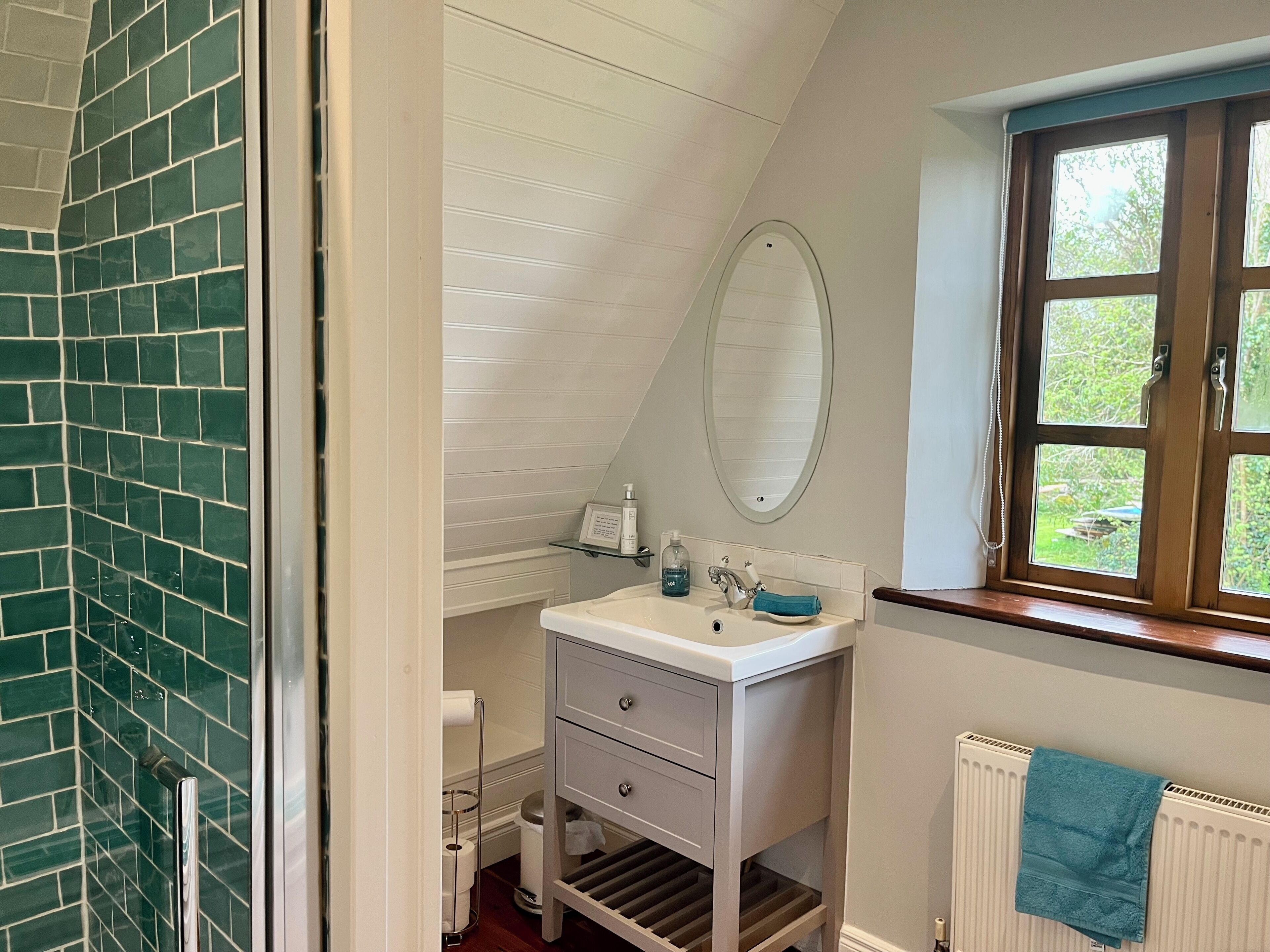 A bathroom with a white sink, a mirror, a towel rack, and a window with a view of greenery.