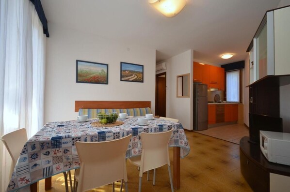 A dining area with a table set for four, a kitchen in the background, and two framed pictures on the wall. - Have a nice stay in a flat with a lovely balcony (Bibione Pineda)