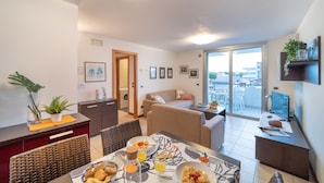 Un salon moderne comprenant un coin repas, un canapé, une table basse et une vue à travers une porte vitrée.