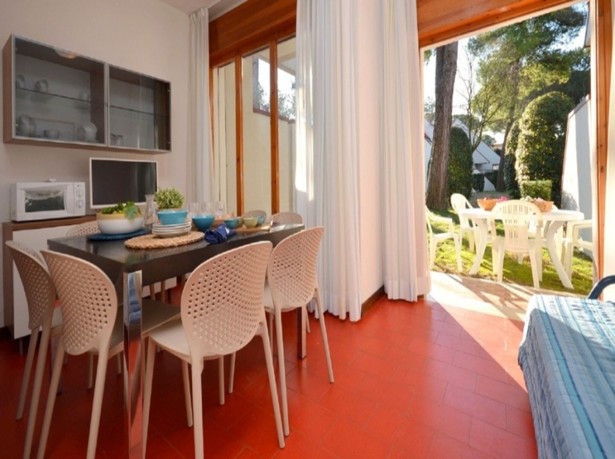A dining area with a table set for four, surrounded by wicker chairs. A microwave and a glass cabinet are visible on the wall.