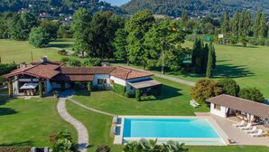 A large house with a swimming pool, surrounded by a well-maintained lawn and trees. - My Rental Homes - Villa Brin with tennis court, private sandy beach and dock (Lesa)