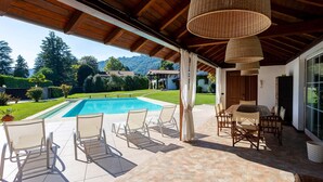 A covered outdoor area with a pool, lounge chairs, and a dining table. - My Rental Homes - Villa Brin with tennis court, private sandy beach and dock (Lesa)