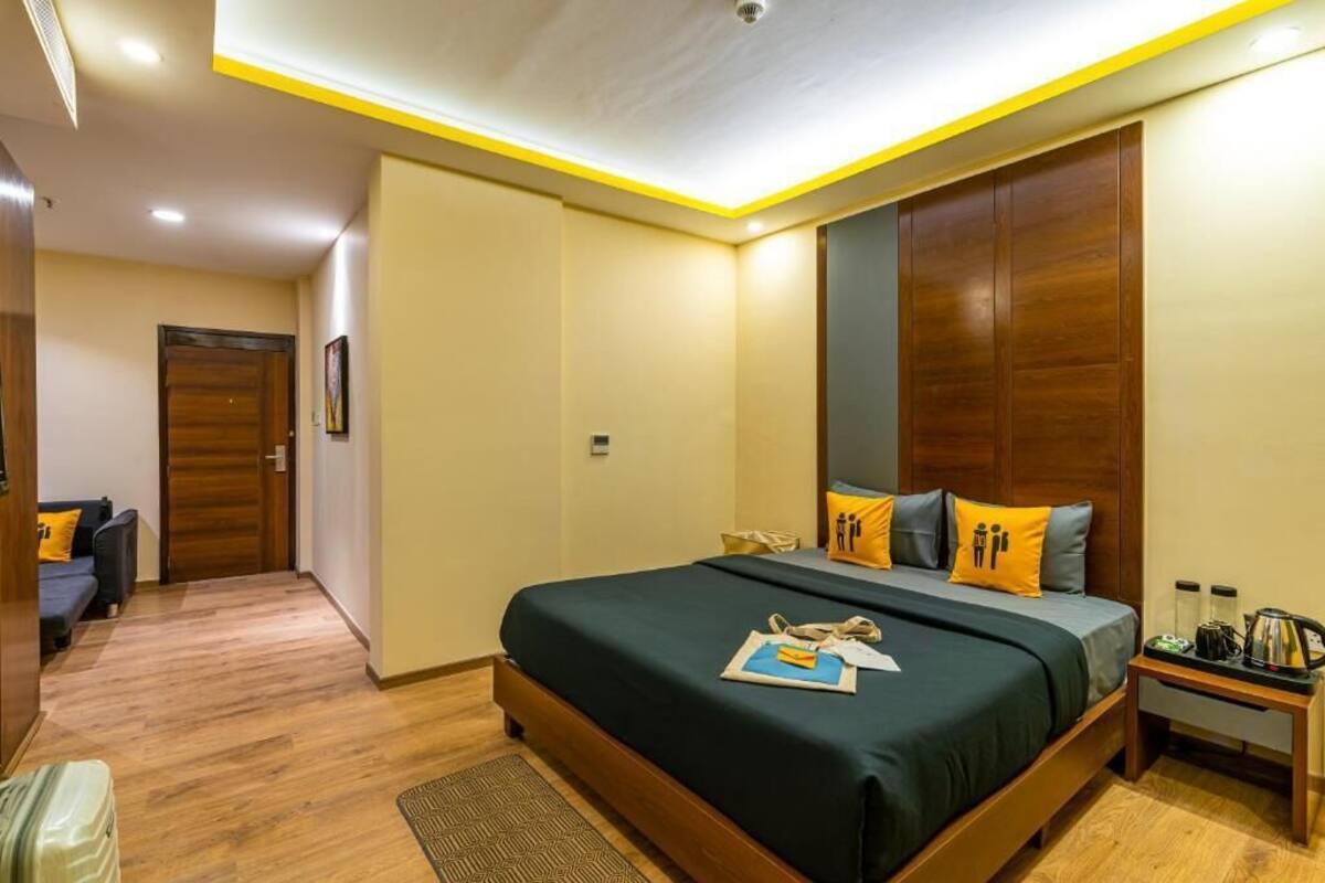 Ein Hotelzimmer mit einem großen Bett, einem Holz-Kopfteil, einem Nachttisch mit Lampe sowie einer kleinen Sitzecke mit Sofa und Kissen.