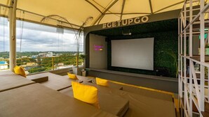 Un salon sur le toit doté d’un grand écran, de coussins jaunes et offrant une vue sur la ville.